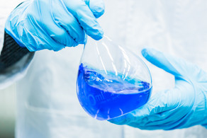 Close-up of volumetric flask Two hands in blue rubber gloves hold a volumetric flask filled with blue liquid.